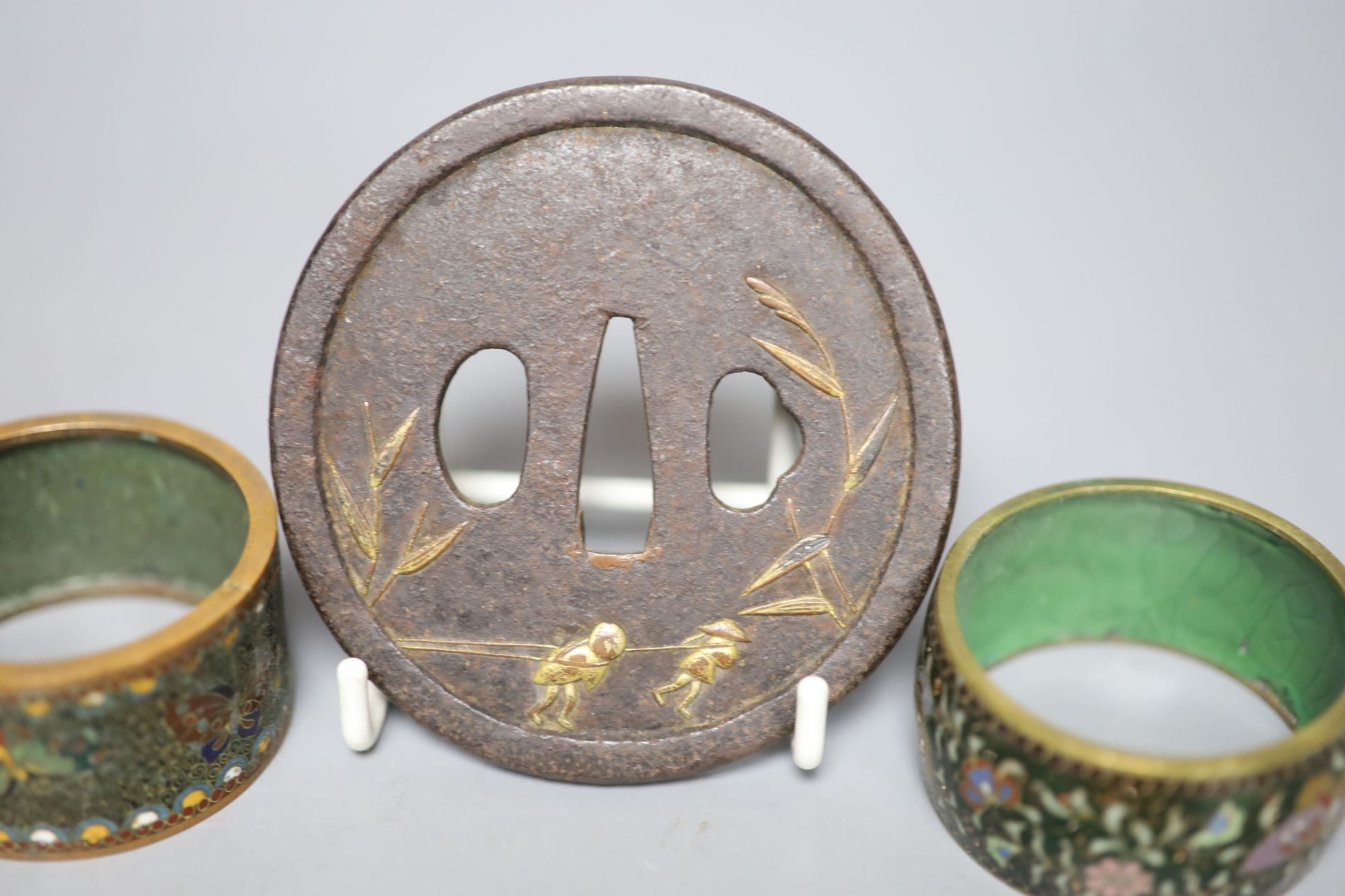 A 19th century Japanese iron and parcel gilt tsuba, unsigned, 8cm and two cloisonne enamel napkin rings.